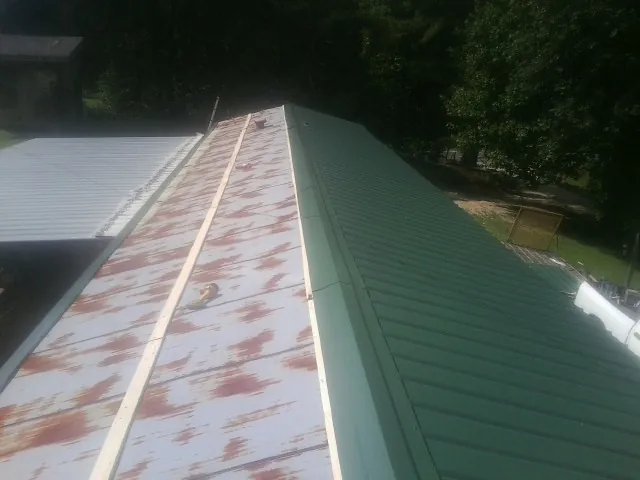 Old rusted panels beside newly installed green metal roofing — Wind Damage Roof Repair by Roofing Brothers in Soldier