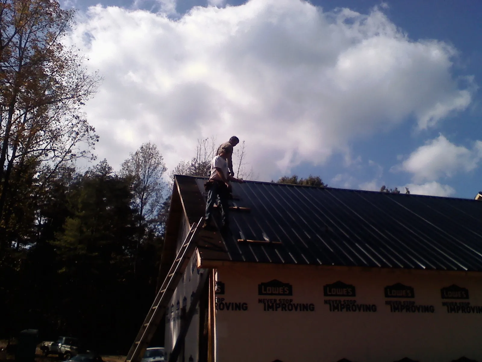 Roofer fastening dark metal panels high against a cloudy sky, from a Roof Inspection job in Soldier