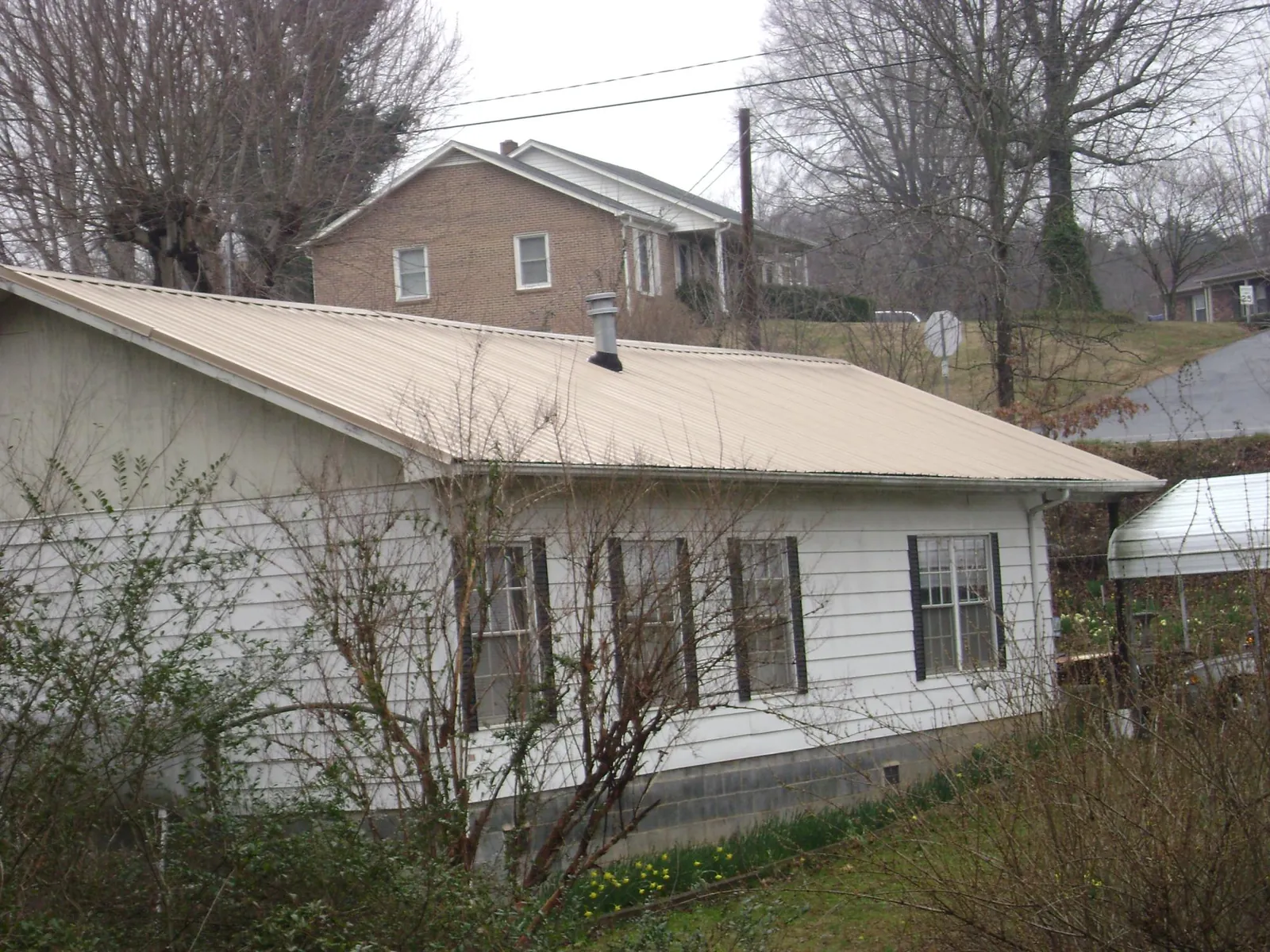 Tan metal roof on a white sided house set into a hillside — Commercial Roofing by Roofing Brothers in Soldier